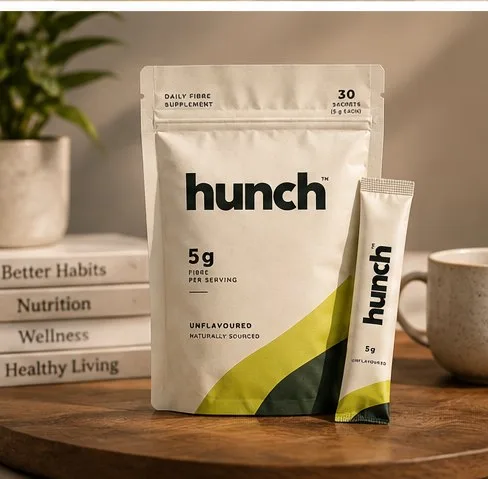 hunch fiber pouch and stick pack next to a stack of habit and nutrition books, with a mug